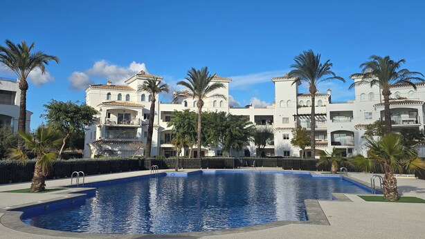 Una piscina rodeada de palmeras y un edificio con balcones.