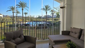 Un balcón con muebles de mimbre, vista a una piscina y palmeras.