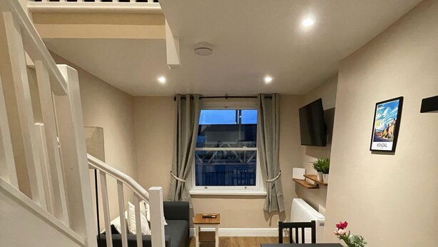 Un espace de vie compact comprenant un escalier, un coin repas, un canapé, un téléviseur et une fenêtre donnant sur un paysage agréable.