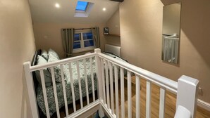 Une chambre avec un plafond en pente, un puits de lumière, un lit avec une literie à motifs, une balustrade blanche et un miroir sur le mur.