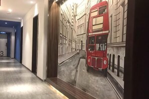 Un pasillo con un mural de un autobús rojo de dos pisos, una puerta con el número 3 y suelo de madera.