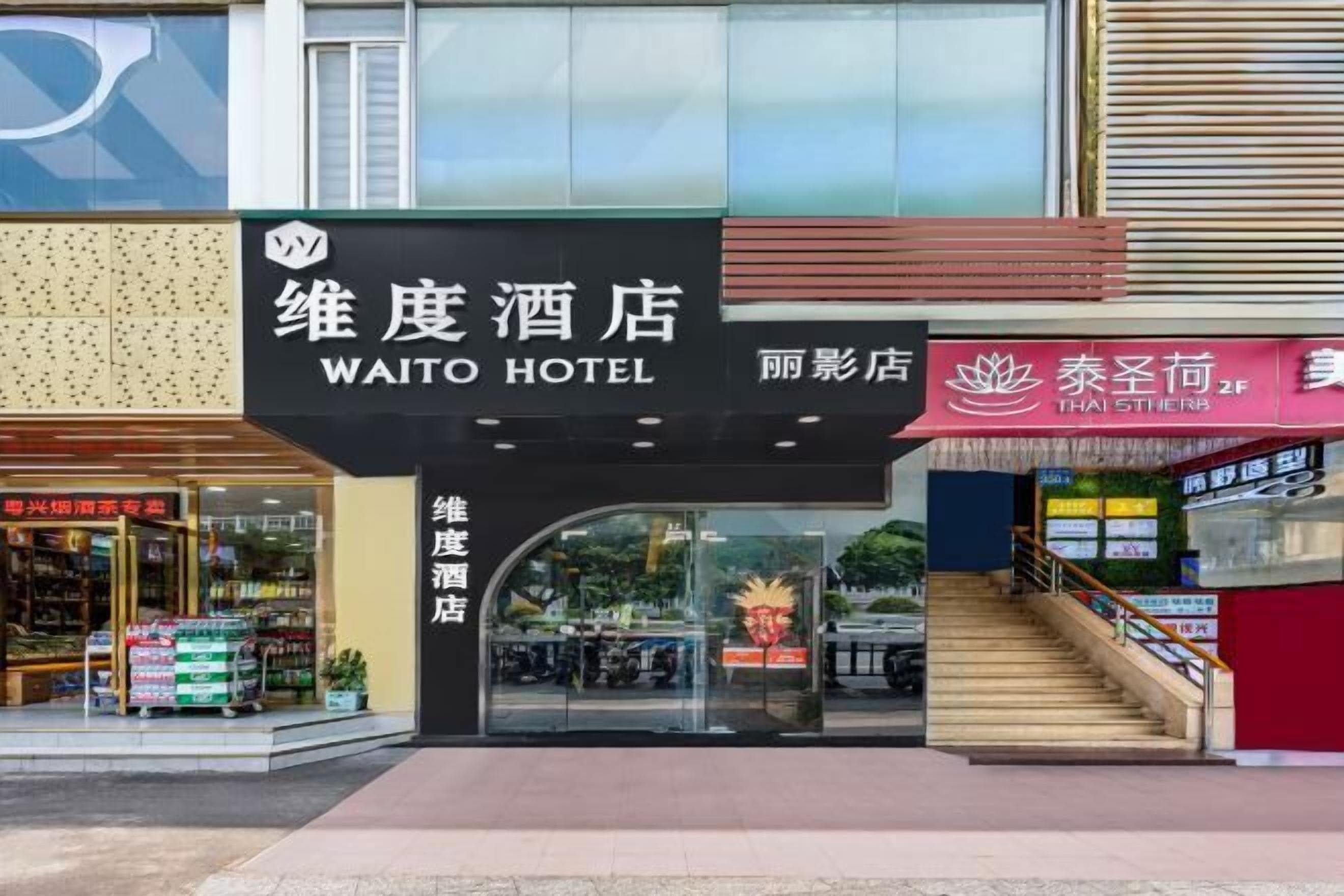 The exterior of the Waito Hotel with a clear entrance, a visible staircase, and a Thai Herb shop adjacent to it.