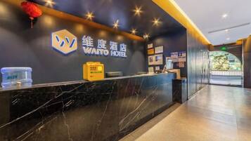 Zona de recepción de un hotel con un mostrador de mármol, un cartel del HOTEL WATTO y vistas al vestíbulo.