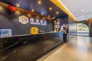 Un espace d’accueil d’hôtel avec un comptoir en marbre, une enseigne indiquant « WATTO HOTEL », et une vue sur le hall d’entrée.