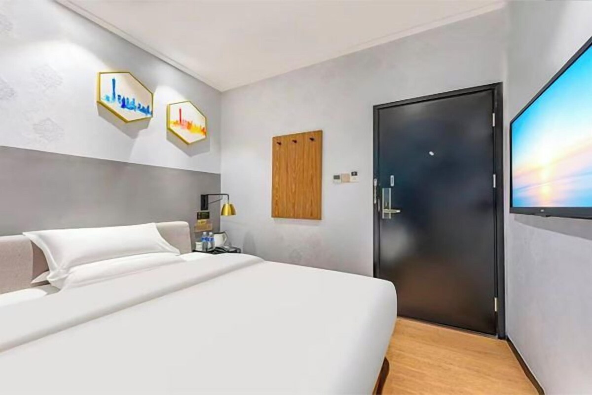 A hotel room with a bed, a desk, a chair, a TV, and a door.