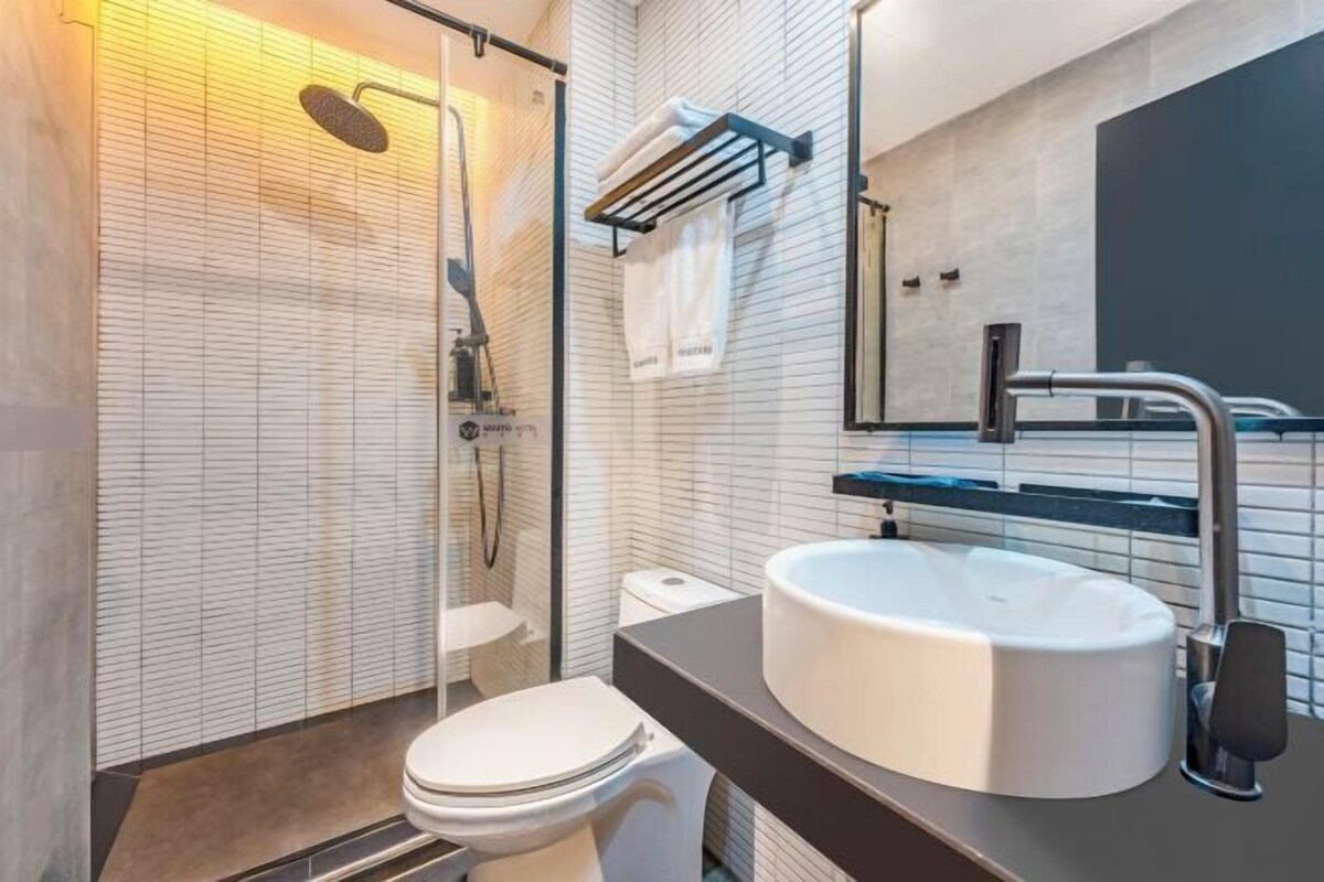 A modern bathroom with a glass shower enclosure, a white toilet, a large round sink, and a mirror above the sink.