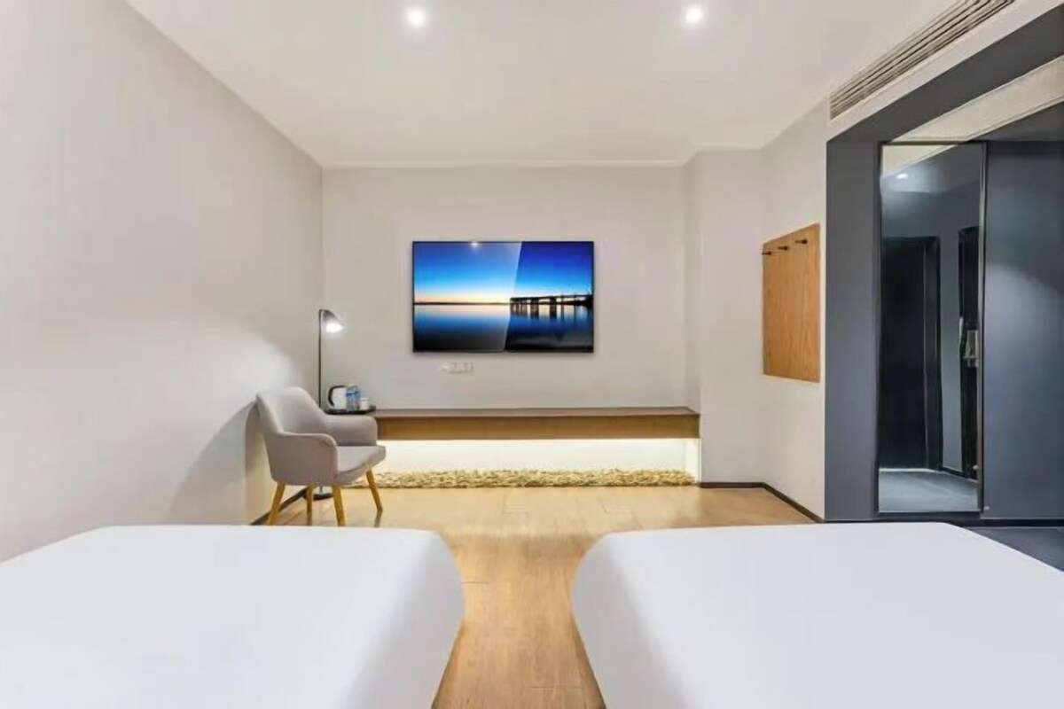 A hotel room with two beds, a TV on the wall, a desk, and a chair.