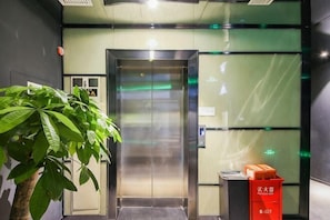 An elevator with a glass panel, a trash bin, and a potted plant.