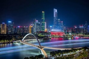 A city skyline at night with illuminated buildings, a prominent bridge, and a river with light trails. - Waito Hotel (Guangzhou Kecun Metro Station Liying Plaza) (Guangzhou)