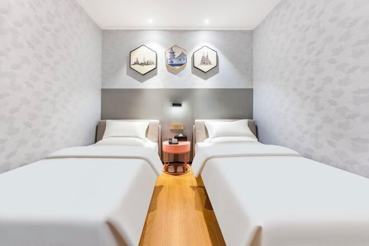 A hotel room with two beds, a small round table, and three hexagonal wall art pieces.