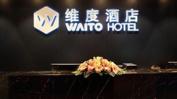 Un comptoir d’accueil avec une enseigne indiquant « HÔTEL WAITO » et un logo au-dessus.