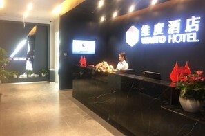 A hotel reception desk with a digital screen, a receptionist, and a sign indicating the hotel name. - Waito Hotel (Guangzhou Kecun Metro Station Liying Plaza) (Guangzhou)