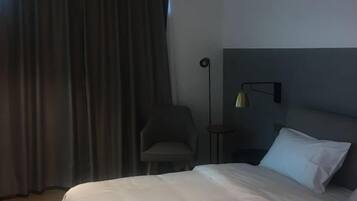 A hotel room with a bed, a chair, a bedside table, and a lamp.