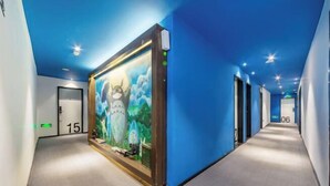 Un couloir d’hôtel avec une grande fresque murale sur le mur de gauche, un sol recouvert de moquette et des portes numérotées 15 et 06.