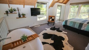 Ein Schlafzimmer mit großem Fenster, einem Bett, einem Fernseher und einer Badewanne.