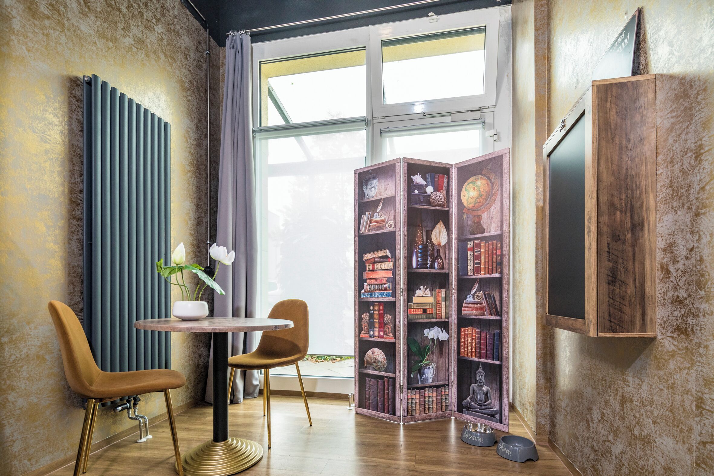 Eine gemütliche Leseecke mit einer Holzbibliothek, zwei Sesseln, einem kleinen Tisch und einer Heizung.