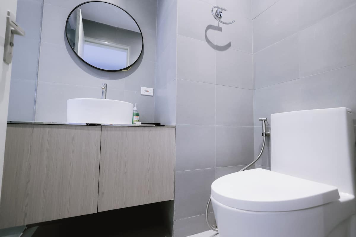 Une salle de bain moderne avec un lavabo blanc, un miroir rond et des toilettes.
