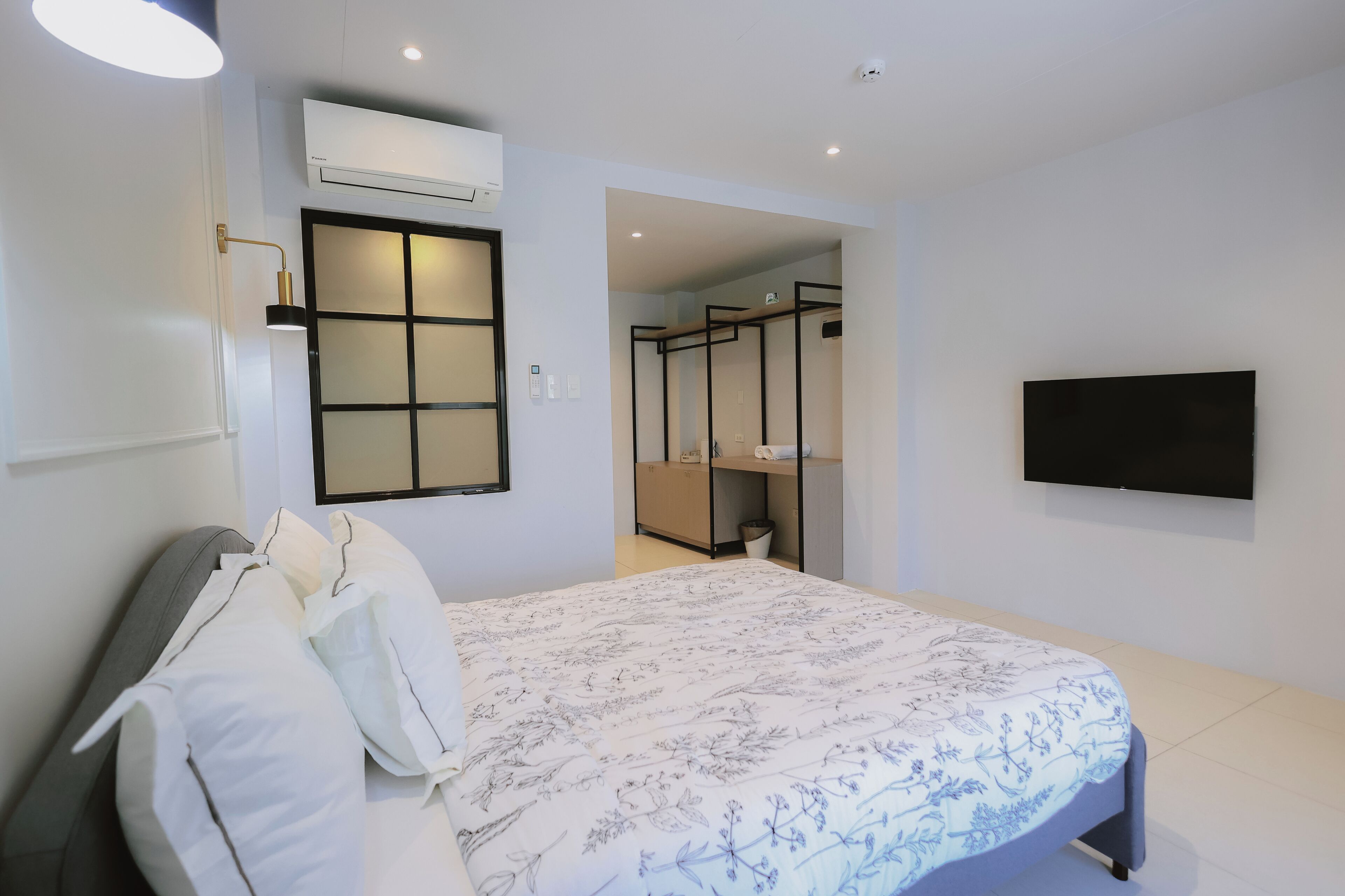 Una habitación de hotel moderna con una cama, un televisor de pantalla plana, un equipo de aire acondicionado y un vestidor.