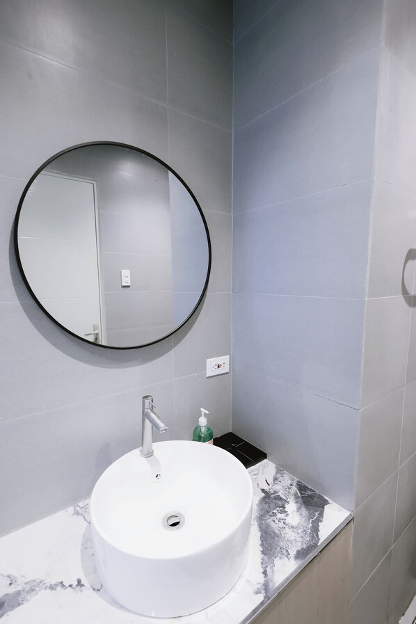 A bathroom with a round mirror, a white sink, and a marble countertop. - Achitel (Tarlac)