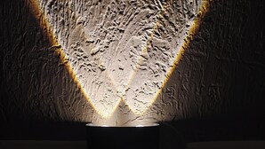 Un mur à texture, avec un luminaire central qui projette des reflets.