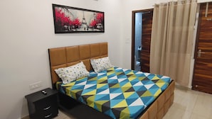 Une chambre à coucher avec un lit, une table de chevet, un ventilateur de plafond, un tableau et une porte avec des rideaux.