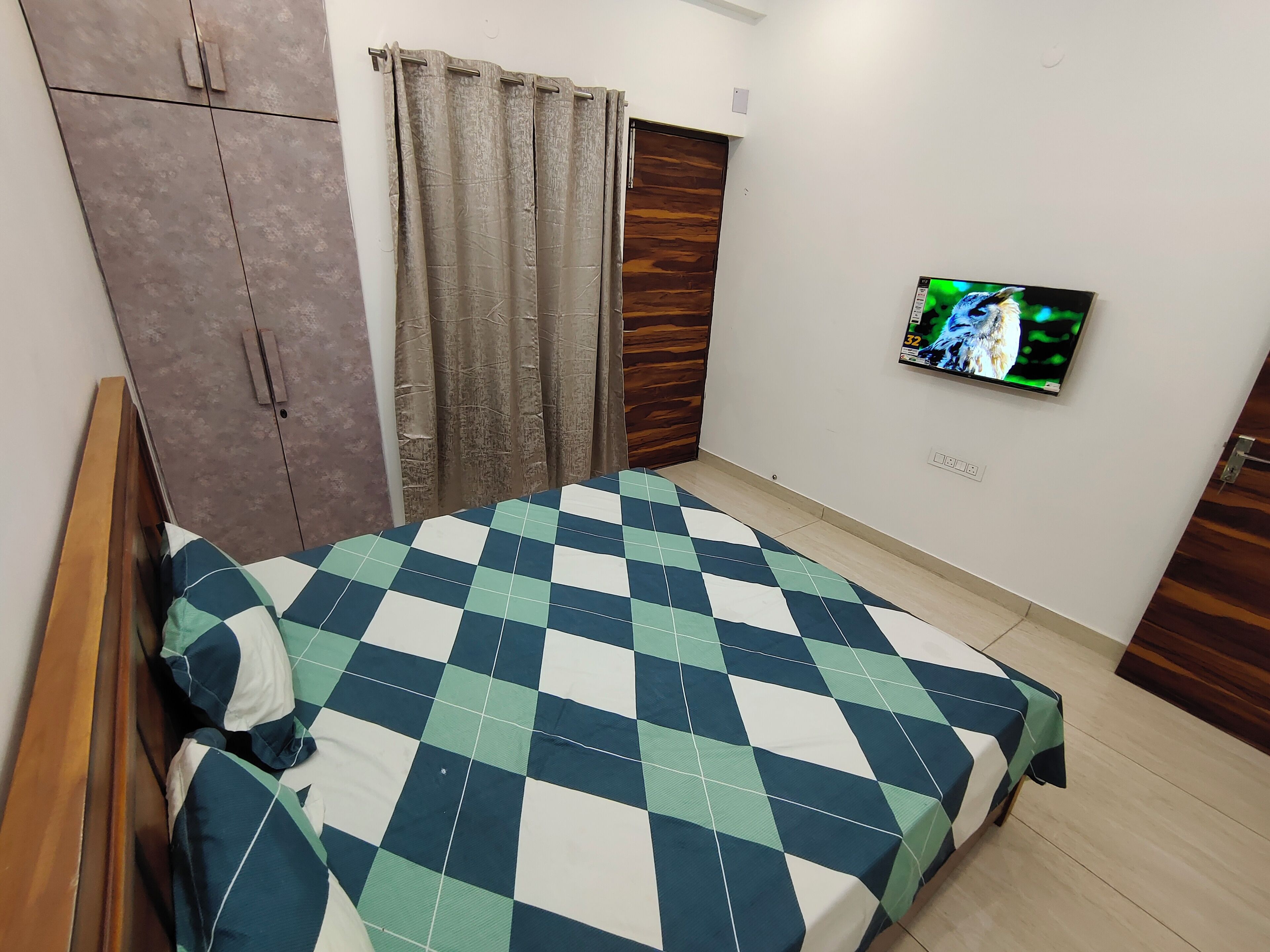 Um quarto com uma cama, um guarda-roupa, uma televisão e uma cortina.