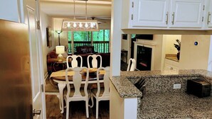 A kitchen with white cabinets, granite countertops, and a dining area with white chairs and a table.