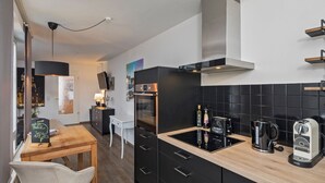 Eine moderne Küche mit schwarzen Schränken, einer Holz Arbeitsplatte, einem eingebauten Ofen, einer Kaffeemaschine und einem Wasserkocher.