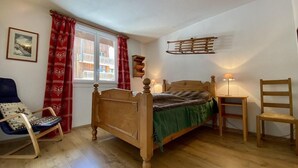 Et soveværelse med en træseng, en gyngestol, et natbord med lampe og et vindue med røde gardiner.