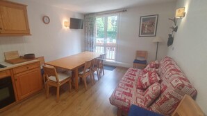 Et kompakt køkken med træskabe, et spisebord med stole og en rød sofa med mønster.