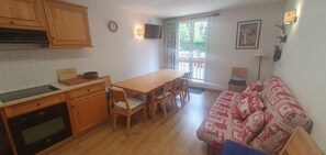 Eine kleine Küche mit Holzausstattung, einem Esstisch mit Stühlen und einem roten, gemusterten Sofa.