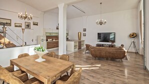 Un vaste espace de vie comprenant une table à manger en bois, un canapé, un téléviseur et un lustre.