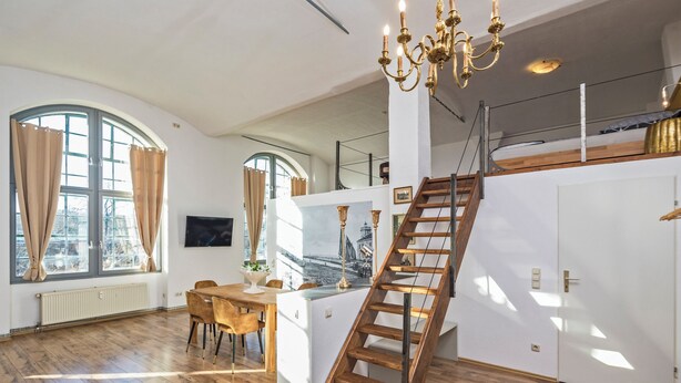 Une pièce spacieuse avec un escalier en bois, un coin repas et de grandes fenêtres dotées de rideaux.