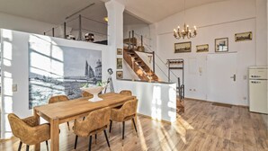 Un vaste espace dédié à la salle à manger, avec une table et des chaises en bois, un escalier menant à un niveau supérieur et un lustre.