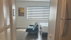 A bedroom with a bed, a chair, a window with blinds, a refrigerator, and a door with louvered panels. - Trendy apartment in Gadsden, AL (Gadsden)