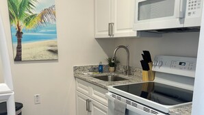 A kitchen with white cabinets, a granite countertop, a stainless steel sink, a microwave, and a stove. - Trendy apartment in Gadsden, AL (Gadsden)