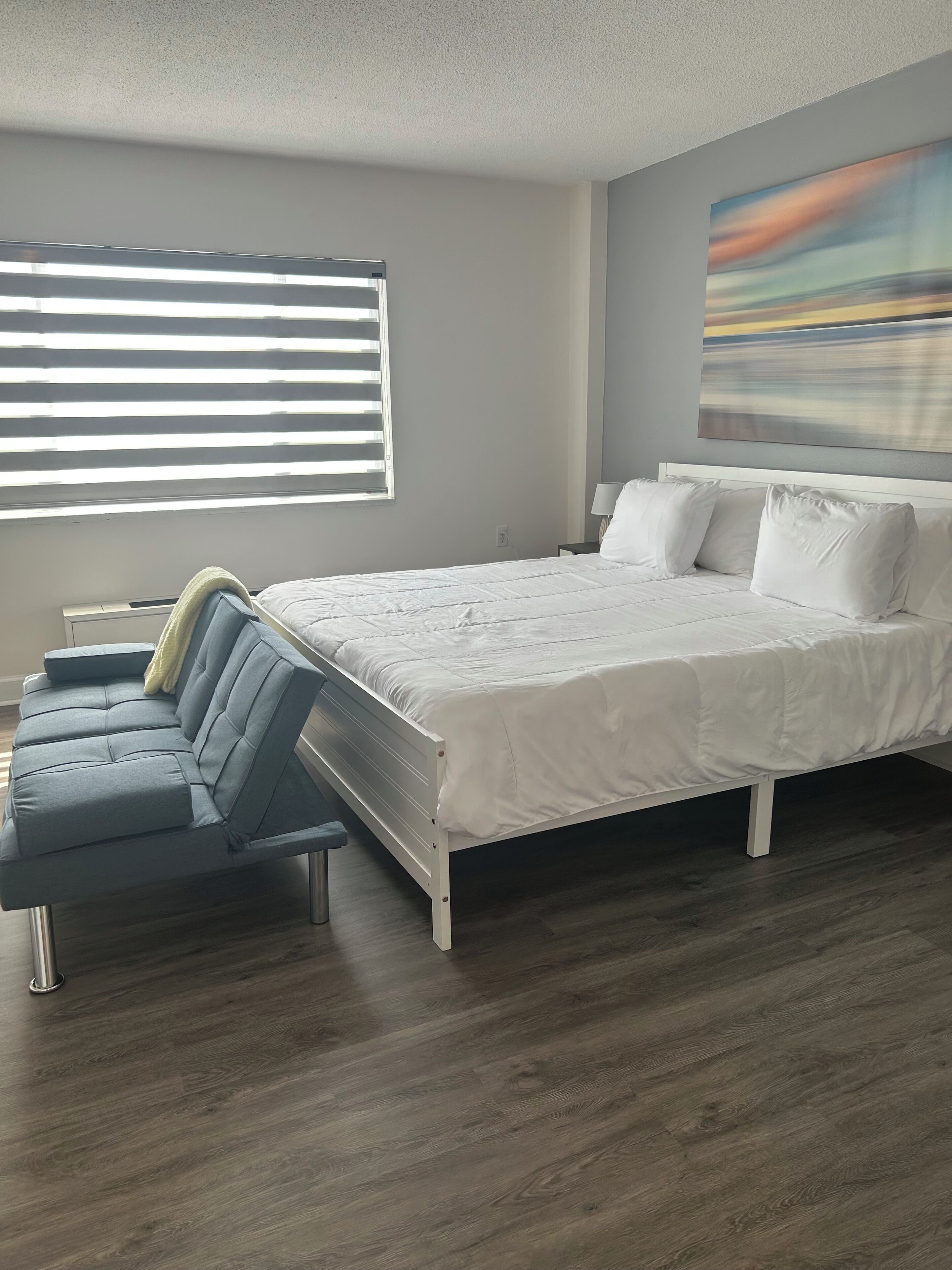 Une chambre moderne avec un grand lit, un canapé et une fenêtre équipée de stores.
