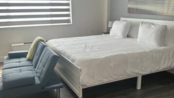 Une chambre moderne avec un grand lit, un canapé et une fenêtre équipée de stores.