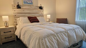 Een slaapkamer met een houten hoofdeinde, twee nachtkastjes met lampen, een bed met witte beddengoed en een raam met zonwering.