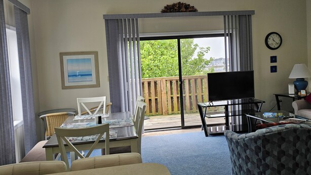 Een hotelkamer met balkon, een zithoek met tafel en stoelen, een bank, een televisie en een klok aan de muur.