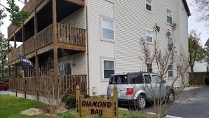 A multi-story residential building with a balcony, a sign reading "Diamond Bay 132", and a parked SUV.