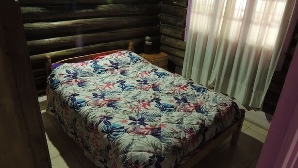 A bed with a floral bedspread in a log cabin room with a wooden headboard and a nightstand. - San Francisco Cabins 1 (Las Vegas)
