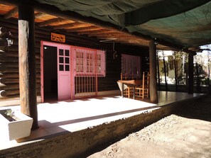 A rustic cabin with a wooden exterior, a pink door, and a covered porch area with a table and chairs. - San Francisco Cabins 1 (Las Vegas)