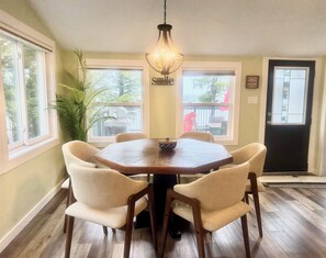 A dining area with a wooden table, six chairs, a hanging light fixture, and a window with a view of the outside.