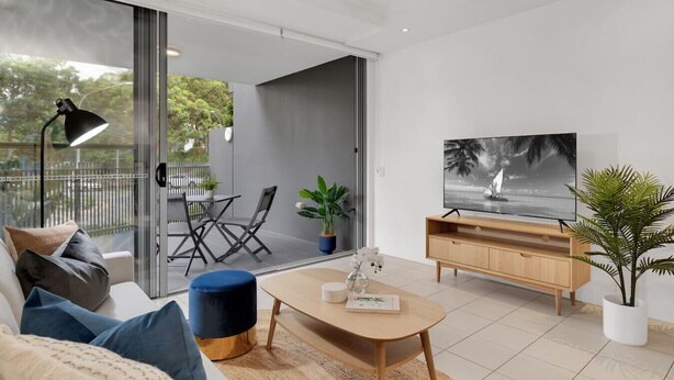 Un salon moderne comprenant un canapé, une table basse, un téléviseur et une porte-fenêtre coulissante donnant sur un espace extérieur avec une table et des chaises.