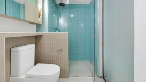 Une salle de bain comprenant des toilettes, une douche et un espace douche délimité par des parois en verre.