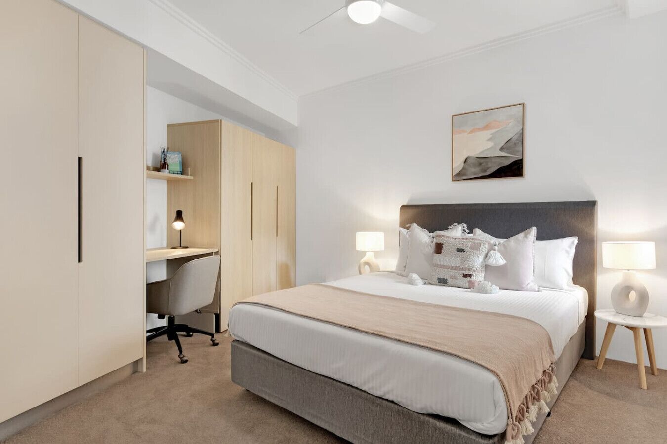 A hotel room with a bed, bedside tables, a desk, and a wardrobe.