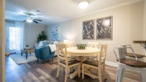 Un comedor con una mesa redonda y sillas, un ventilador de techo y decoración en la pared.