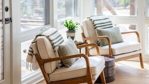 Dos sofás de madera con cojines color beige y almohadas a rayas, ubicados cerca de un ventanal con vistas al exterior.