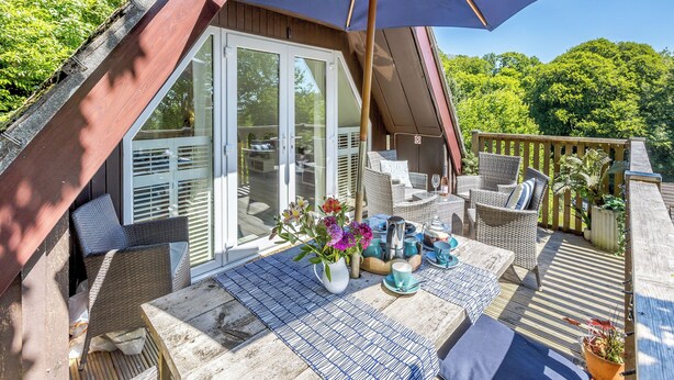 An outdoor patio with a table set for dining, surrounded by wicker furniture and a large umbrella. - Valley Lodge - UK49228 (Gunnislake)